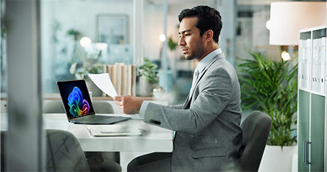 man on microsoft laptop looking at a peice of paper